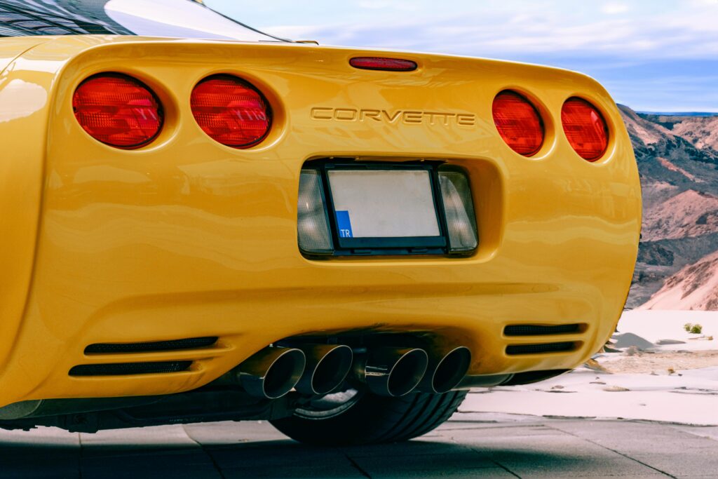 Close-up of a yellow Corvette on a scenic road, highlighting sleek design and performance.