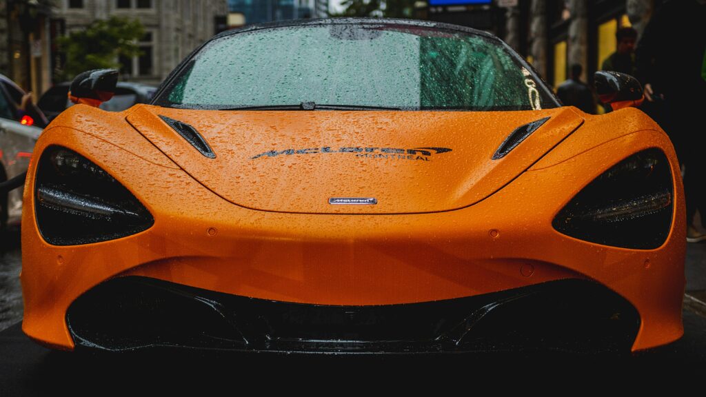 Front view of a McLaren 720S with raindrops in an urban setting, showcasing luxury car design.