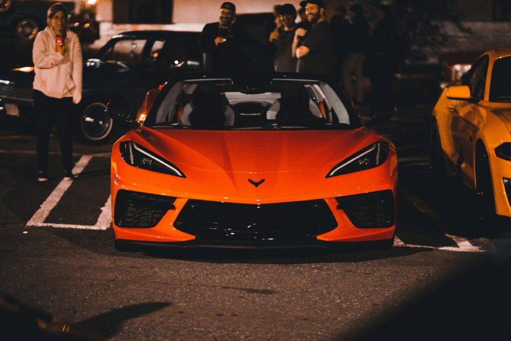 Vibrant red Chevrolet sports car parked at a nighttime car meet with a crowd in the background.